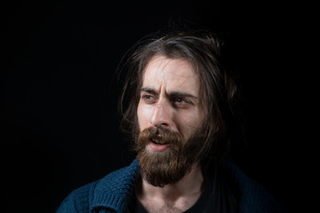 Young man with long hair with hippie type long beard, surprised face, in black isolated background.