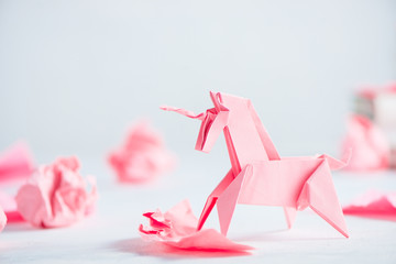 Pink origami unicorn with crumpled paper balls. Creative process is writing, light background - obrazy, fototapety, plakaty