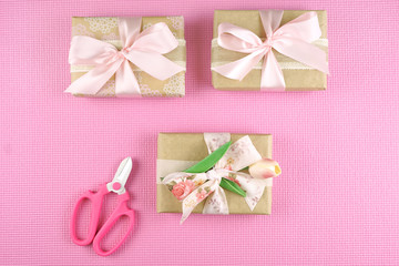 Gifts wrapped in kraft paper and pink ribbons overhead flat lay for Mother's Day, birthday or Valentine's Day celebrations.