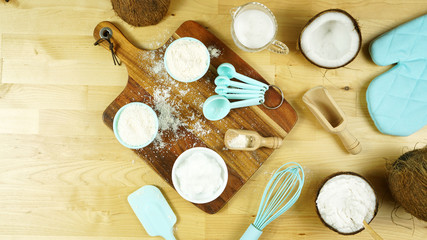 Fototapeta na wymiar Coconut baking theme flat lay creative layout overhead with coconut flour, milk, oil, and shredded desiccated coconut and baking utensils on modern wooden table. Negative copy space.