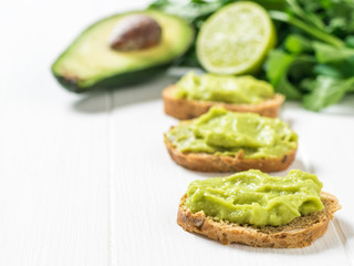 Pieces of grain bread with guacamole on a wooden table. Diet vegetarian Mexican food avocado.