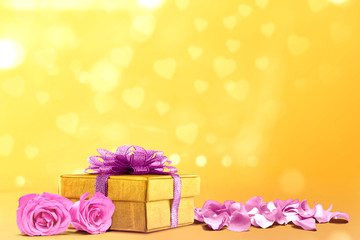 Gift box and pink rose petals on a yellow background