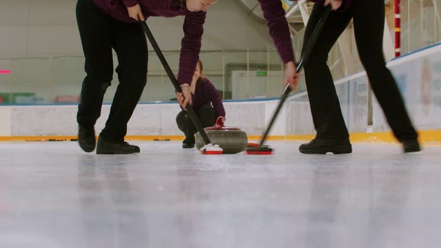 Curling training indoors - rubbing the ice before the biter - third woman watching other players
