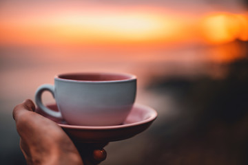 Person holding a coffee cup in hand at amazing sundown.
