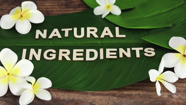 Natural Ingredients message on tropical banana leaf with monoi frangipani flowers with camera panning vertically