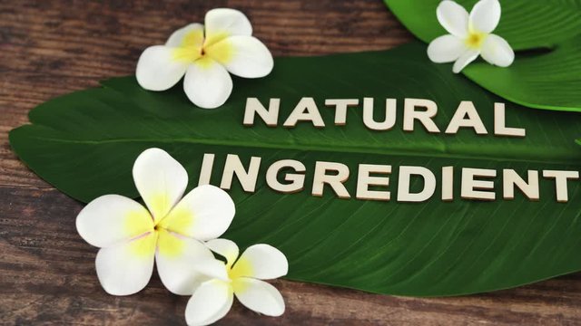 Natural Ingredients message on tropical banana leaf with monoi frangipani flowers with camera panning horizontally