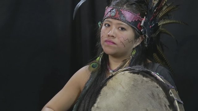 close up of young woman Teotihuacana, Xicalanca - Toltec in black background, with traditional dress dance with a trappings with feathers and drum