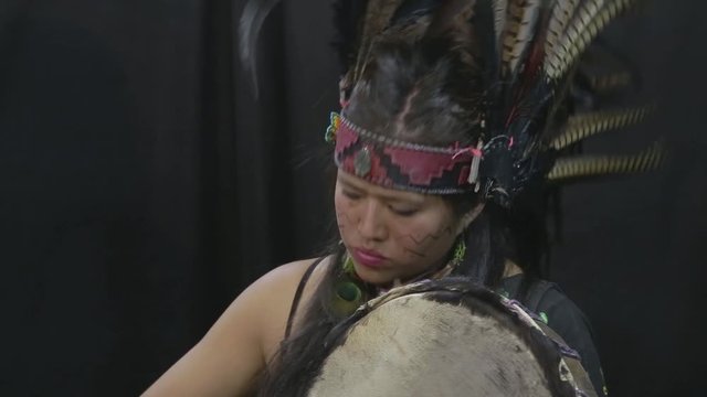 close up of young woman Teotihuacana, Xicalanca - Toltec in black background, with traditional dress dance with a trappings with feathers and drum