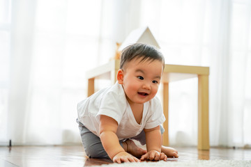One lovely male infant laughing and having fun in living room against white windows. He can sit on the floor in living room at home.