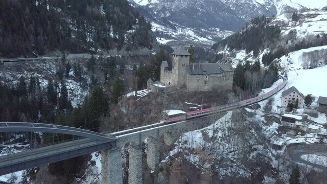Flying with the drone over a castle and over a bridge, a train is crossing the bridge, The landscape looks like in winter wonderland.