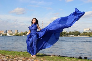 A woman in a long blue classic dress that fluttered in the wind, selective focus. River