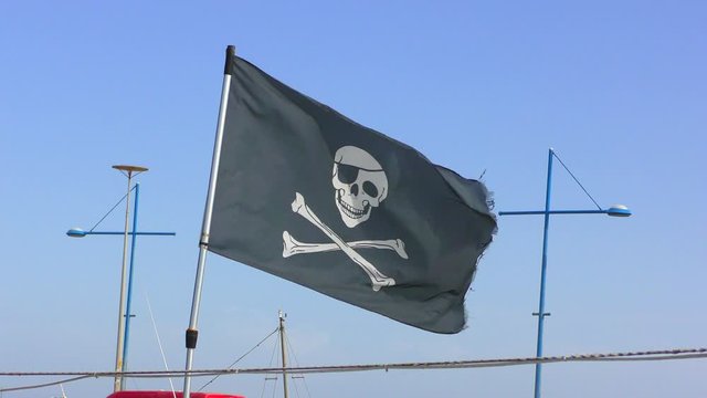A pirate flag on a mast of a pleasure boat flies against a blue sky