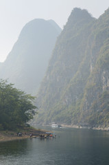 Cruise ship and sightseeing rafts on the hazy Li River in China among the tall karst peaks of Guangxi