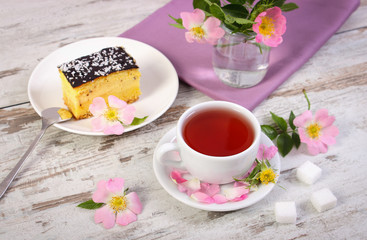 Cup of tea with cheesecake and wild rose flower on old wooden background