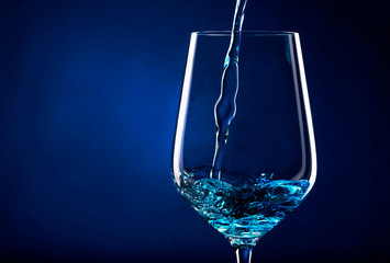 Blue wine, trendy non-classical wine drink pouring into glass on blue background