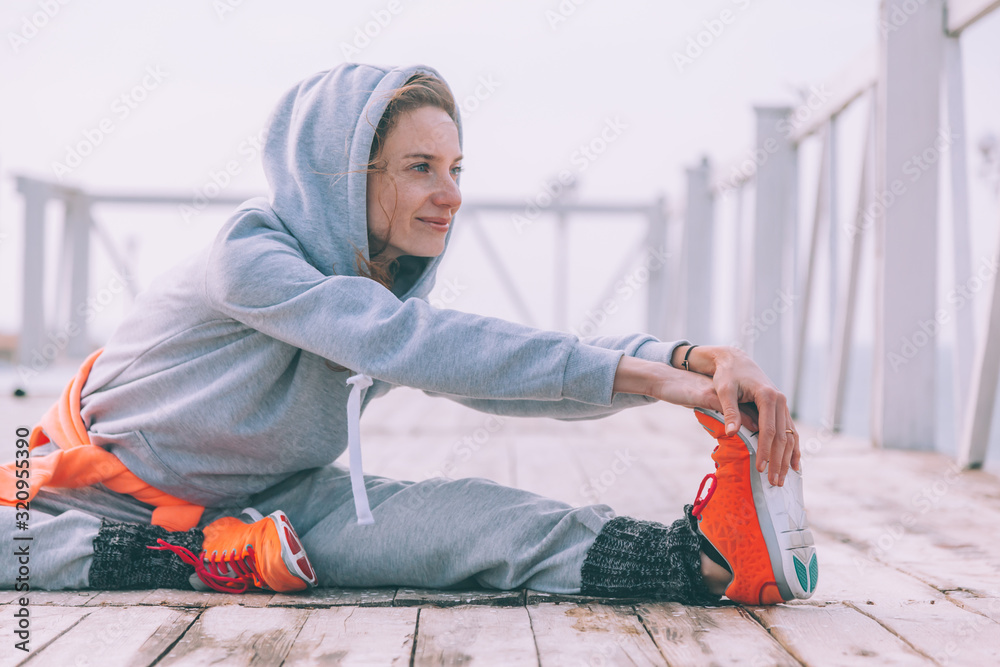 Wall mural Fitness sport girl in fashion sportswear doing yoga fitness exercise in the street by sea