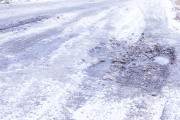 The bad asphalt winter road or way with ice, snow, puddles, pools, mud and slush