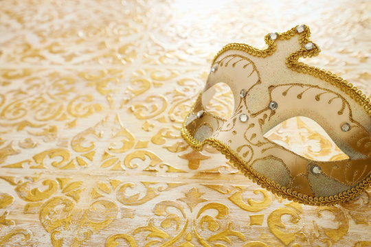 Photo of elegant and delicate Venetian mask over vintage gold wooden background