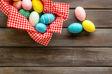 Basket with painted eggs for Easter dinner on dark wooden desk top-down copy space