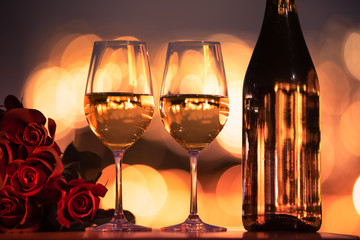 two glasses of wine and bottle of wine on wooden table with roses