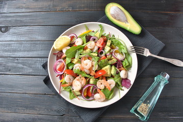 Avocado salad with shrimps, cherry tomatoes, arugula beet leaves, red onion, yellow sweet pepper. Healthy lunch plate with vegetables and shrimps