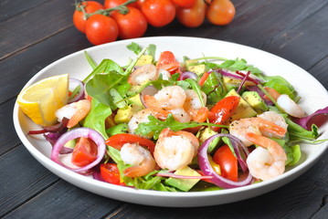 Avocado salad with shrimps, cherry tomatoes, arugula beet leaves, red onion, yellow sweet pepper. Healthy lunch plate with vegetables and shrimps