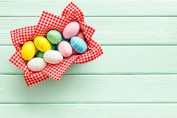 Easter eggs painted in basket on green wooden desk top-down copy space