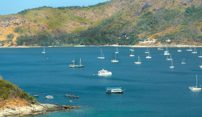 Obraz premium Many white boats and boats in the sea bay surrounded by rocks and islands, with hotels and houses on the banks of the green bank.
