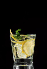Cold drink on a black background. One glass with lemonade or mojito cocktail with lemon and mint. Copy space, close up.