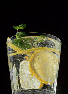 Cold drink on a black background. One glass with lemonade or mojito cocktail with lemon and mint. Close up