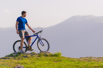Obraz premium Fit mountain biker riding his bike through green grass on top of a mountain.