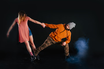 Fototapeta na wymiar Couple dancing modern dance and showing off their leg stretch moves.Black background while the couple is dressed in urban colorful clothes...