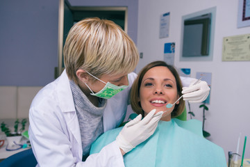 Female dentist in dental office examines the mouth and teeth of a female patient