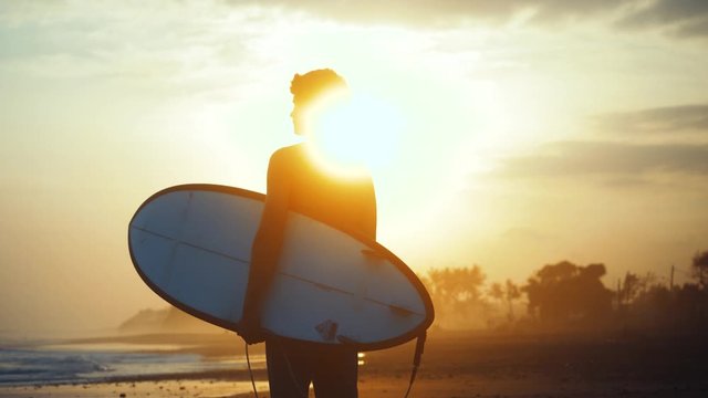 SLOW MOTION Adventure travel athletic man with surfboard enjoying evening at the beach
