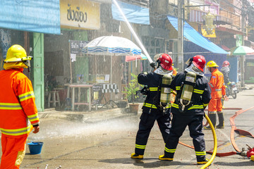 Obraz premium Firefighters of Lampang city confederate water spray and control the hoses to quench the fire in the real annual rehearsal fire drill in urban city.