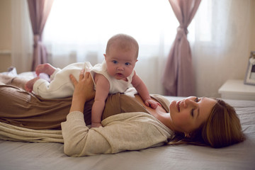 young mother with red hair is lying on the bed with her daughter