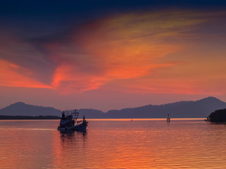 Fototapeta na wymiar Sea view evening of fishing boat running in the sea with red sun light and cloudy sky background, twilight at Kuraburi Pier, Phang Nga, southern of Thailand.