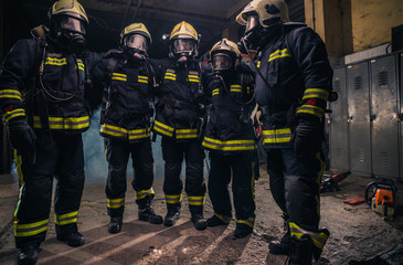 Team of firemen in uniform with gas masks inside the fire department