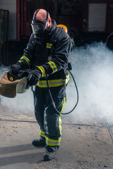 Portrait of a fireman wearing firefighter turnouts and helmet. Dark background with smoke and blue light.