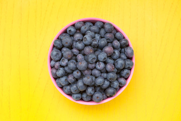 blueberries in pink bowl on yellow table