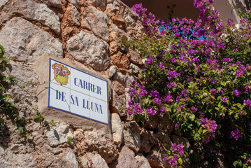Typisches mediterranes Stra&szlig;enschild aus Fliesen der "Mondscheingasse" auf Baleareninsel Mallorca an einem alten Steinhaus mit Bougainvillea