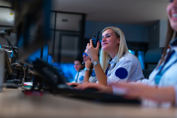 Happy security data center operator colleagues (coworkers) smiling and monitoring the CCTV footage while typing on a keyboard.