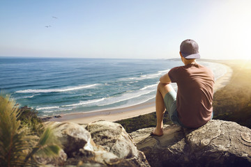 Young man sitting on a rock above a beautiful coastline - Powered by Adobe