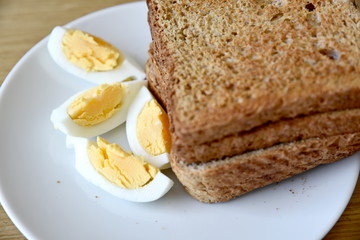 Whole wheat slice toasted bread with sliced boiled egg on the white plate for breakfast
