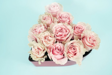 Delicate pink roses in the shape of a heart. Flowers in a designer basket on a mint background