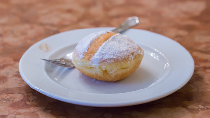 An original austrian Krapfen (also: Berliner, a kind of doughnut) served on a plate. A sweet speciality in german speaking countries. Popular food during carnival.