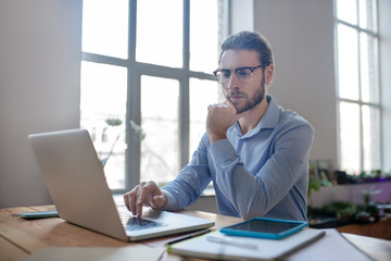 Young smart man with glasses looking at a laptop.