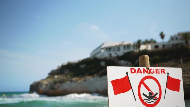 Danger, no swimming sign with red flags, blurred windy sea waves in background