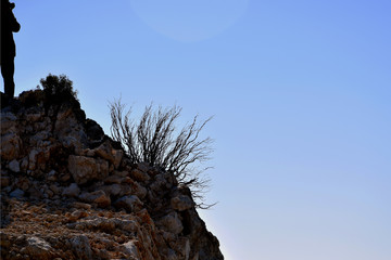 View of single rock and photographer on the top, who is taking pictures, blue sky background