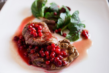Close up view of the beef steak with lingonberry dressing, beet leaves on the white plate. Delicious food, lunch or dinner.